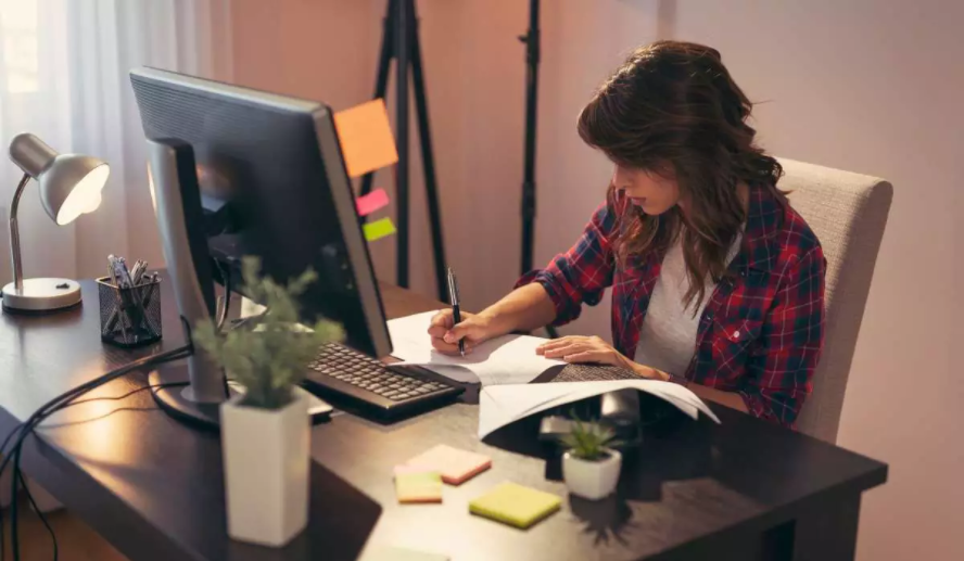 Mulher trabalhando em um computador e realizando anotações em um caderno